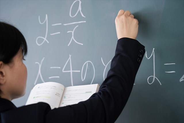教室で黒板に文字を書く日本人女性教師